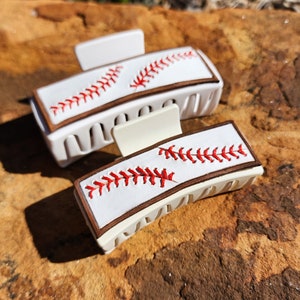 A 4inch and 3.5inch white claw clips. Both have the same leather piece on them that resemble baseball. There is a brown border with white background and red stitches