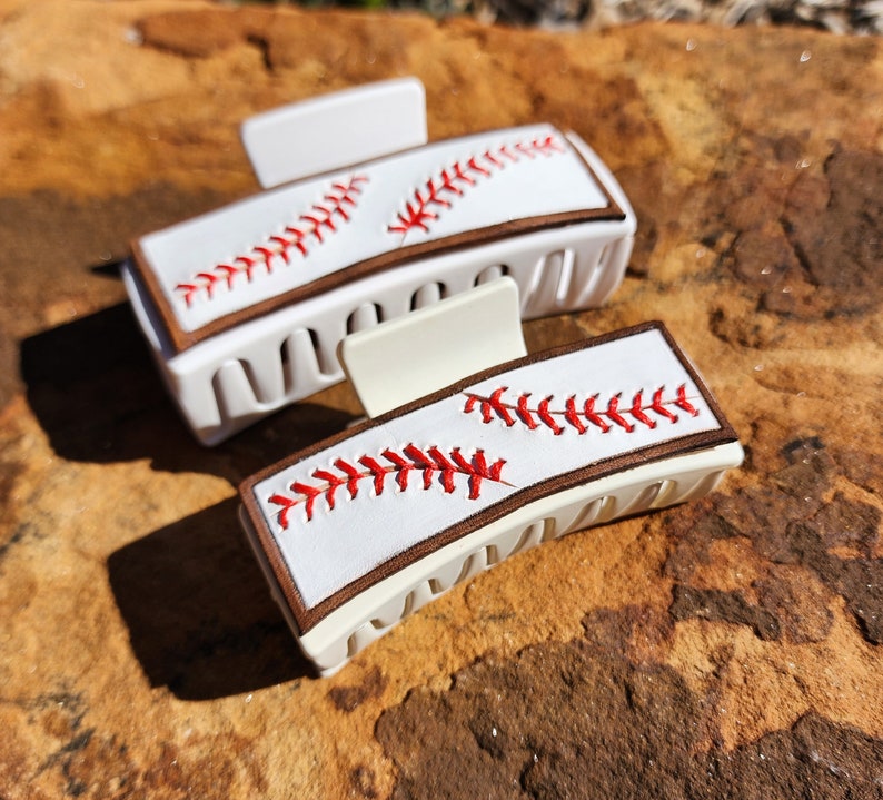 A 4inch and 3.5inch white claw clips. Both have the same leather piece on them that resemble baseball. There is a brown border with white background and red stitches