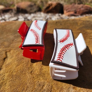 Two clips, one is white and the other red. Both are 4inch and have a leather piece on them that resemble a baseball. There is a brown border with white background and red stitches