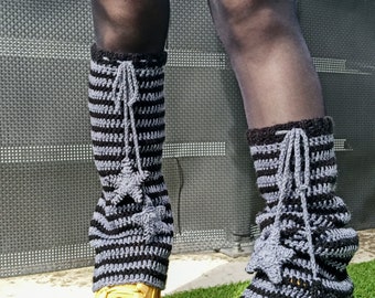 May include: A pair of black and gray striped crochet leg warmers with a tassel detail. The leg warmers are worn over black tights and paired with tan platform sneakers.