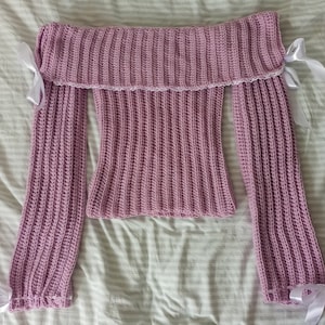 Peut inclure: Un pull en crochet mauve à épaules dénudées avec des manches longues et des liens en ruban blanc aux épaules.