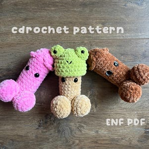 Könnte beinhalten: Drei handgefertigte Häkel-Penis-Spielzeuge in Rosa, Beige und Braun, mit schwarzen Knopfaugen. Eines hat einen grünen Froschhütchen. Der Text "cdrochet pattern" und "ENF PDF" sind sichtbar.
