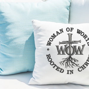 May include: White throw pillow with a black embroidered design of a cross with nails, the letters "WOW" and roots. The text around the design reads "Woman of Worth Rooted in Christ".