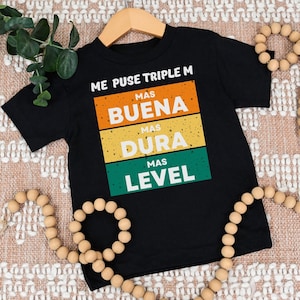 May include: Black t-shirt with a colorful graphic that says "Me puse triple M mas buena mas dura mas level".