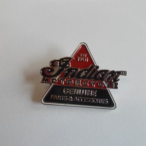 May include: A red and black triangular pin with the words "Indian Motorcycle" and "Genuine Parts & Accessories" in white lettering. The pin also includes the text "Est. 1901" in white lettering.