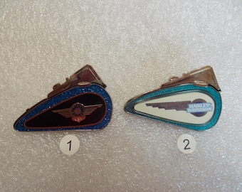 Peut inclure: Deux épingles en forme de réservoir de moto Harley-Davidson. L'une est noire avec une bordure pailletée bleue et le logo Harley-Davidson. L'autre est blanche avec une bordure pailletée turquoise et le logo Harley-Davidson.