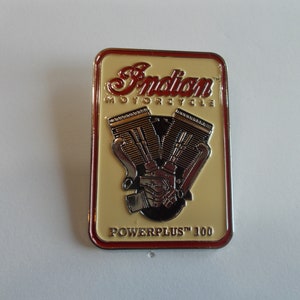 May include: A red, white, and silver metal pin with the words "Indian Motorcycle" and "PowerPlus 100" on it. The pin features a stylized image of a motorcycle engine.