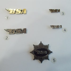 May include: Five silver and gold coloured metal pins with the word "BSA" on them. The pins are arranged in a grid pattern on a white background.