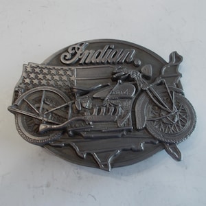 Könnte beinhalten: Eine silberne Gürtelschnalle mit einer detaillierten Darstellung eines Indian-Motorrads mit dem Wort "Indian" darüber. Das Motorrad ist vor dem Hintergrund einer amerikanischen Flagge dargestellt.