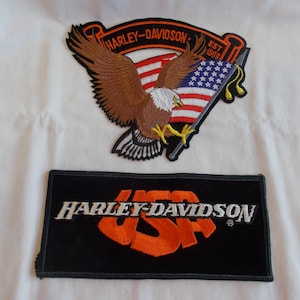 May include: Two Harley-Davidson embroidered patches. The top patch features a brown eagle holding an American flag with the text "Harley-Davidson" and "Est. 1903". The bottom patch is black with the text "Harley-Davidson" in white and "USA" in orange.