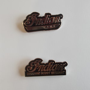 May include: Two silver metal Indian Motorcycle logo pins. The top pin says "Indian" with "Spirit" underneath. The bottom pin says "Indian" with "Scout" underneath.