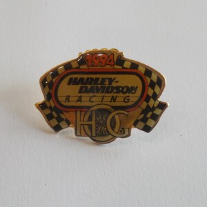 May include: A gold-colored pin with a black and white checkered border. The center of the pin features a red and orange oval with the text "1994 Harley-Davidson Racing H.O.G."