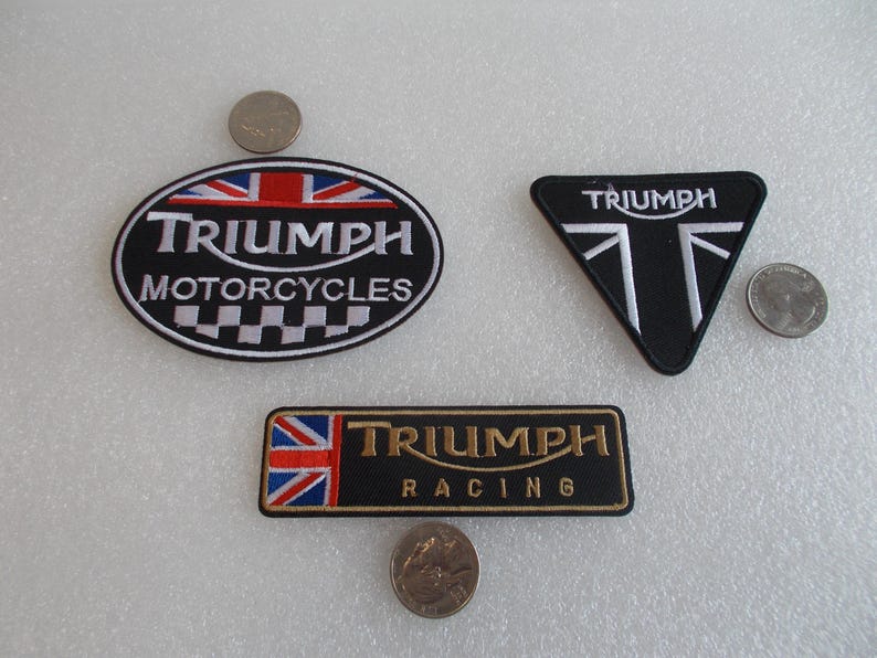 K&ouml;nnte beinhalten: Drei gestickte Triumph-Aufn&auml;her. Einer ist oval mit "Triumph Motorcycles" und einem Union-Jack-Design. Ein weiterer ist ein schwarzes Dreieck mit dem Triumph-Logo. Der dritte ist rechteckig mit "Triumph Racing".