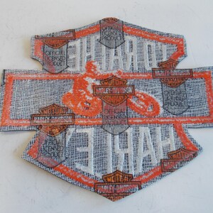 May include: A Harley-Davidson patch with a textured, gray background and orange and white accents. The patch features the Harley-Davidson logo and the words "HARLEY-DAVIDSON" and "OFFICIAL LICENSED PRODUCT".