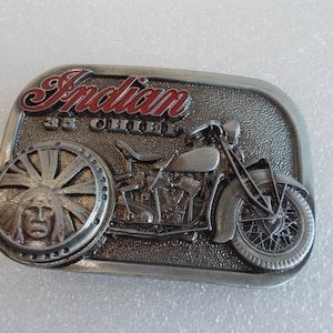 Könnte beinhalten: Silberne Gürtelschnalle mit einem detaillierten 3D-Bild eines Vintage-Indian 35 Chief Motorrads. Das Motorrad ist silberfarben mit roten Akzenten und einem schwarzen Reifen. Die Schnalle zeigt auch einen indianischen Kopf mit einem Federkopfschmuck.