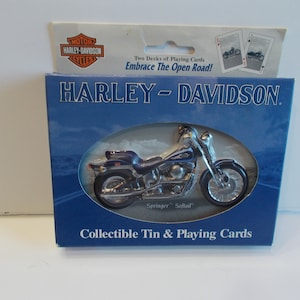 May include: A blue and silver Harley-Davidson motorcycle collectible tin with two decks of playing cards. The tin features a picture of a Harley-Davidson motorcycle with the text "Springer Softail" underneath. The text "Collectible Tin & Playing Cards" is printed on the bottom of the tin.