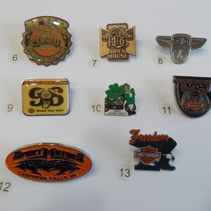 May include: A collection of 10 Harley Davidson motorcycle pins. The pins are various shapes and sizes and feature different designs, including a motorcycle, a shamrock, and a bald eagle. The pins are all metal and have a shiny finish.