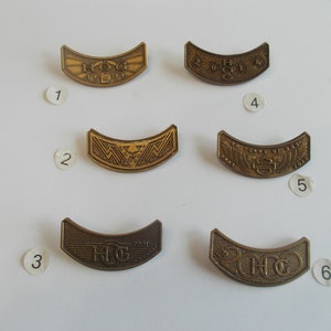 May include: A selection of six vintage Harley-Davidson HOG pins. Each pin is a curved, bronze-coloured metal badge. The pins feature various designs, including the HOG logo, years, and other decorative elements. These pins are likely collectible items.