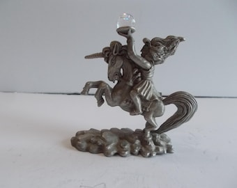 May include: A pewter figurine of a fairy riding a unicorn, holding a crystal ball. The unicorn is rearing up on its hind legs, and the fairy is wearing a flowing dress. The figurine is set on a base that resembles clouds.