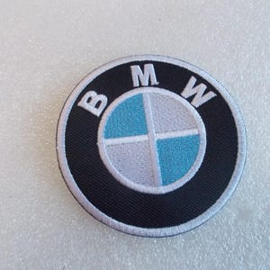 Pode incluir: Um emblema bordado circular com o log&oacute;tipo da BMW. O design inclui um anel exterior preto com as letras brancas B, M e W, e um c&iacute;rculo central dividido em quatro quadrantes com cores alternadas azul-claro e branco.