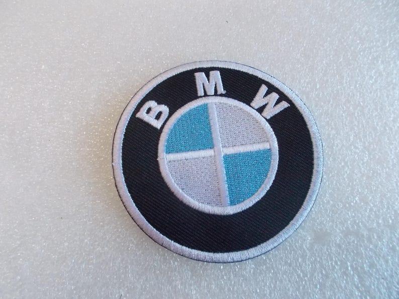 Pode incluir: Um emblema bordado circular com o log&oacute;tipo da BMW. O design inclui um anel exterior preto com as letras brancas B, M e W, e um c&iacute;rculo central dividido em quatro quadrantes com cores alternadas azul-claro e branco.