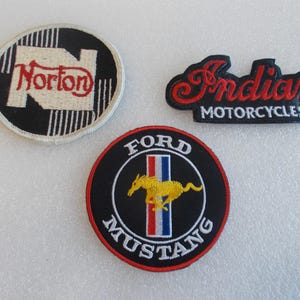 May include: Three embroidered patches featuring classic automotive and motorcycle brands. Includes a black and white Norton patch, a red and black Indian Motorcycles patch, and a Ford Mustang patch with a yellow horse.