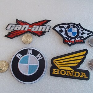 Pode incluir: Quatro emblemas bordados com logotipos automotivos e de esportes motorizados. Um emblema Can-Am em vermelho, preto e branco. Um emblema BMW Racing Sport com design de bandeira quadriculada. Um emblema circular BMW. Um emblema Honda com asa amarela.