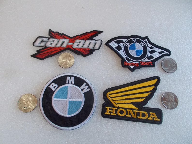 Pode incluir: Quatro emblemas bordados com logotipos automotivos e de esportes motorizados. Um emblema Can-Am em vermelho, preto e branco. Um emblema BMW Racing Sport com design de bandeira quadriculada. Um emblema circular BMW. Um emblema Honda com asa amarela.