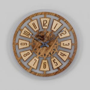 May include: A round wooden wall clock with a light brown finish. The clock face features a clear glass cover and a decorative wooden frame with cut-out numbers. The clock hands are silver. The clock measures approximately 12 inches in diameter.