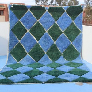 May include: A large, rectangular rug with a diamond pattern in shades of blue and green. The rug has a white border.