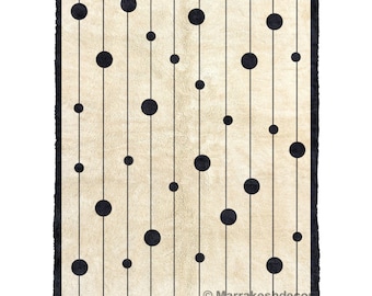 May include: A beige rug with a black geometric pattern of circles and lines. The rug has a fringe border.
