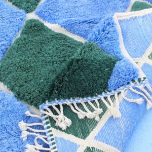 May include: A blue and green geometric patterned rug with a fringe border. The rug is made of soft, fluffy fibers.