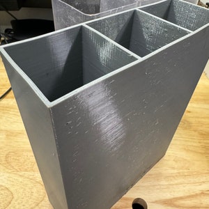 May include: A gray plastic organizer with three compartments. The organizer is made of a textured plastic and has a slightly rough surface.