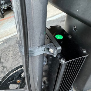 May include: A black electric bike motor with a green sticker that says "QC" mounted to a black metal frame. The motor has a black heatsink with fins.