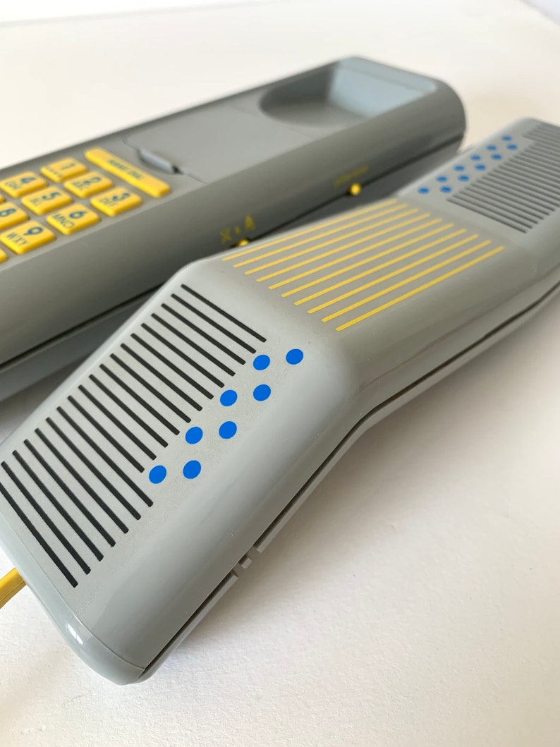 May include: A gray rotary phone with a yellow keypad and blue dots. The phone has a gray and yellow striped design on the receiver.