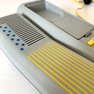 May include: A gray rotary phone with a yellow and blue design. The phone has a built-in answering machine and a cord.