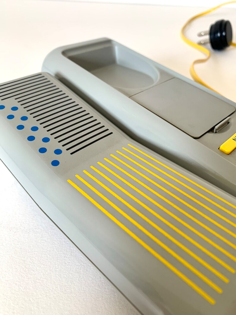May include: A gray rotary phone with a yellow and blue design. The phone has a built-in answering machine and a cord.