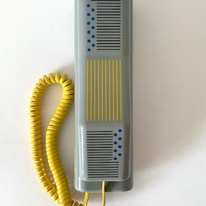 May include: A gray rotary phone with a yellow coiled cord. The phone has a geometric design with black and blue lines and dots.