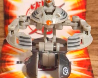 Könnte beinhalten: Eine graue und dunkelgraue Bakugan-Spielfigur mit einem zentralen humanoiden Kopf mit orangefarbenen Akzenten, beweglichen Armen mit dreistreifigen Details und einer kugelförmigen Basis mit einem kreisförmigen Emblem mit einem fünfzackigen Stern.