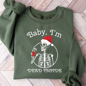 May include: Green sweatshirt with a white graphic of a skeleton wearing a Santa hat and holding a red cup. The text "Baby, I'm Dead Inside" is printed below the skeleton.