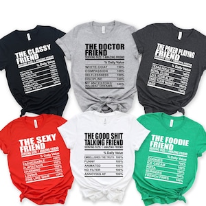 May include: Six different t-shirts with humorous friend titles and descriptions. The shirts are in various colours, including red, white, green, grey, and black. Each shirt has a different title, such as "The Classy Friend", "The Doctor Friend", "The Poker Playing Friend", "The Sexy Friend", "The Good Shit Talking Friend", and "The Foodie Friend".