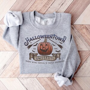 May include: Gray sweatshirt with a Halloweentown University graphic. The graphic features a jack-o'-lantern, bats, a broom, and the text "Halloweentown University est. 1998" and "Where being normal is vastly overrated".