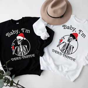 May include: Two black and white sweatshirts with a skeleton wearing a Santa hat and holding a cup. The text on the sweatshirts reads "Baby, I'm Dead Inside".