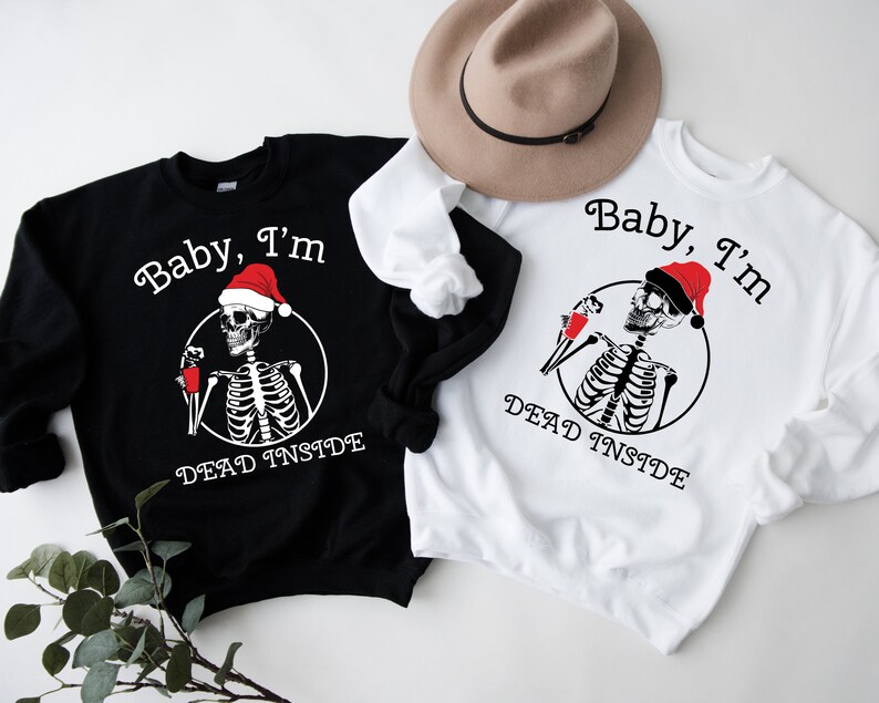 May include: Two black and white sweatshirts with a skeleton wearing a Santa hat and holding a cup. The text on the sweatshirts reads "Baby, I'm Dead Inside".