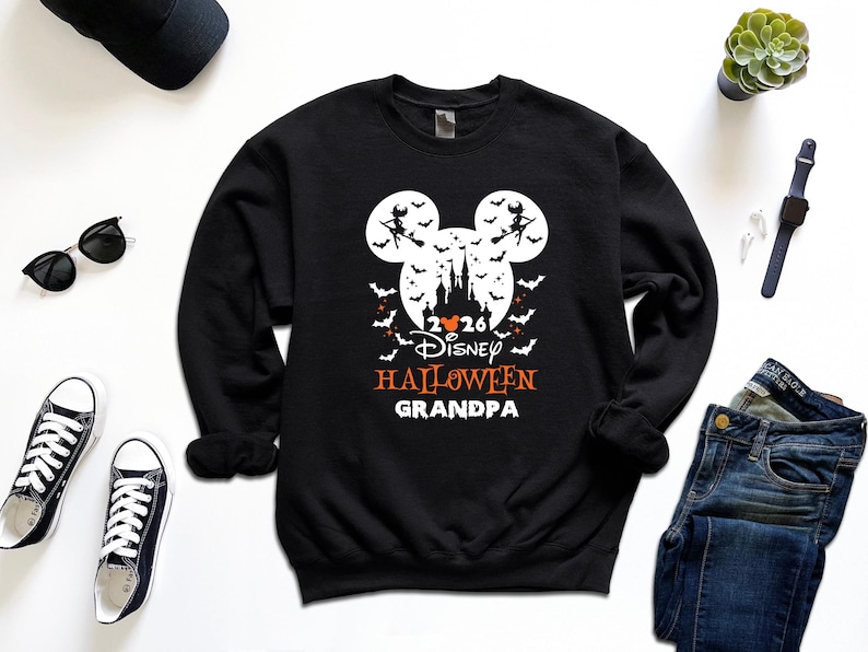 May include: A black long-sleeve sweatshirt featuring a white graphic of a castle silhouette inside a Mickey Mouse head shape, surrounded by bats and witches. The text reads 2026, Disney, HALLOWEEN, and GRANDPA in white and orange lettering.