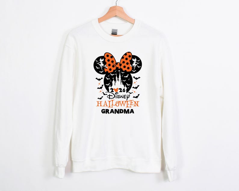 May include: A white long-sleeve sweatshirt featuring a black and orange graphic of Mickey Mouse ears with a polka dot bow, a castle silhouette, bats, and the text 2026 Disney HALLOWEEN GRANDMA printed in black and orange on the front centre.