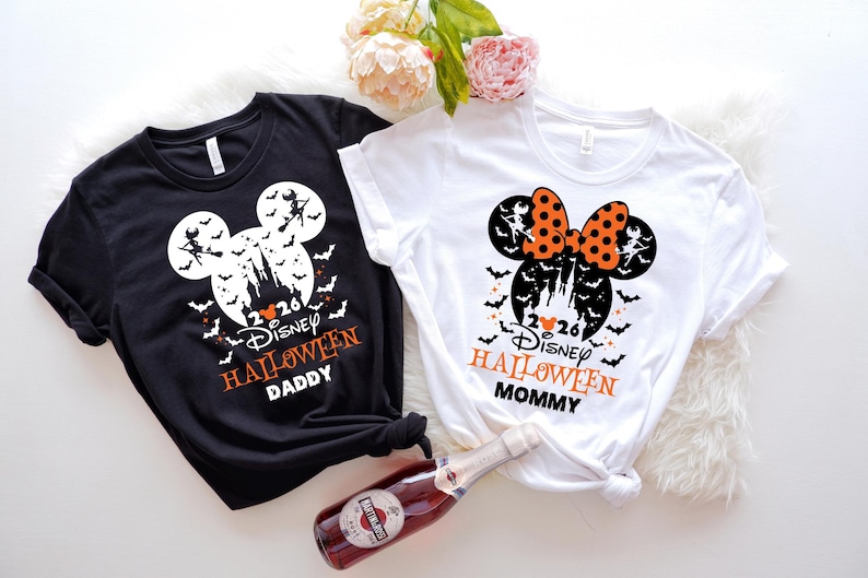 May include: A black t-shirt and a white t-shirt featuring a Mickey Mouse silhouette graphic with a castle, bats, and a witch on a broomstick. The text reads 2026 Disney HALLOWEEN DADDY on the black shirt and 2026 Disney HALLOWEEN MOMMY on the white shirt.