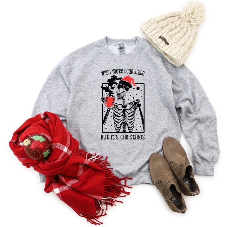 May include: A gray sweatshirt with a black and white illustration of a skeleton wearing a Santa hat and holding a mug. The text "When you're dead inside but it's Christmas" is printed on the sweatshirt.