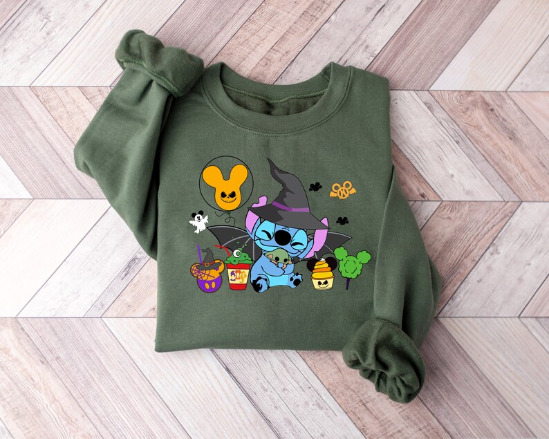 May include: Green sweatshirt with a blue Stitch character wearing a witch hat and holding a small green alien. The design includes a Mickey Mouse balloon, a ghost, and other Halloween-themed elements.