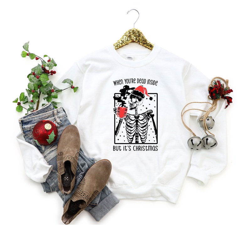 May include: White sweatshirt with a black and white illustration of a skeleton wearing a Santa hat and holding a cup of coffee. The text "When you're dead inside but it's Christmas" is printed on the sweatshirt.